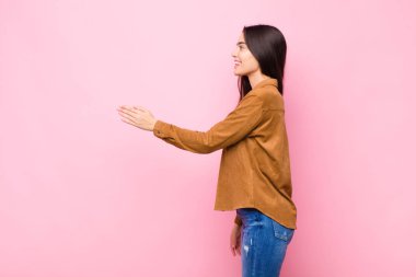 Genç, güzel bir kadın gülümsüyor, seni selamlıyor ve başarılı bir anlaşma için el sıkışmayı teklif ediyor. Pembe duvara karşı işbirliği konsepti.