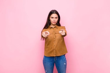 Genç ve güzel bir kadın kameraya iki parmağını ve kızgın bir ifadeyle bakıyor ve sana pembe duvara karşı görevini yapmanı söylüyor.