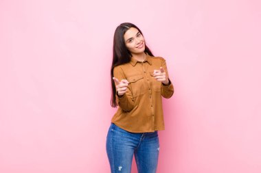 Genç, güzel bir kadın, olumlu, başarılı, mutlu bir tavırla kamerayı işaret ederek, pembe duvara el işareti yaparak,
