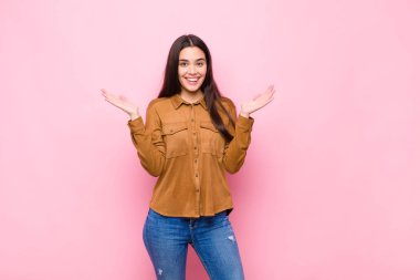 Genç, güzel bir kadın mutlu ve heyecanlı görünüyor. Beklenmedik bir sürprizle şoke olmuş gibi. İki eli yüzü pembe duvara dönük.