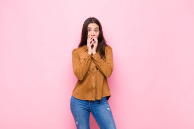 Genç, güzel bir kadın endişeli, üzgün ve korkmuş hissediyor. Elleriyle ağzını kapatıyor. Endişeli görünüyor ve pembe duvara karşı her şeyi berbat ediyor.