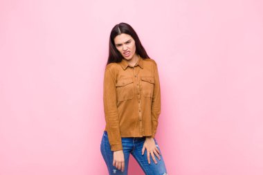 Genç ve güzel bir kadın şaşkın ve şaşkın hissediyor, aptal, şaşkın bir yüz ifadesiyle beklenmeyen bir şeye bakıyor pembe duvara karşı.