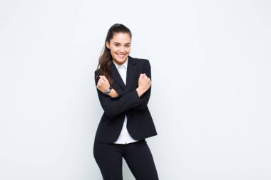 Genç ve güzel bir kadın, neşeli bir şekilde gülümsüyor ve kutluyor. Yumruklarını sıkmış, kollarını kavuşturmuş, mutlu ve pozitif iş kavramını hissediyor.