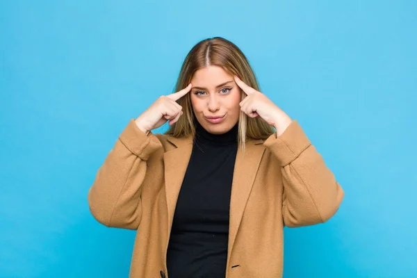 young blonde woman with a serious and concentrated look, brainstorming and thinking about a challenging problem against flat wall