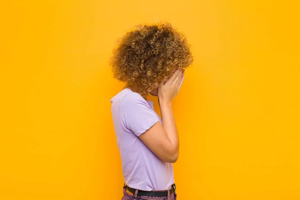 悲しみに満ちた絶望の表情で手で目を覆い泣いている若いアフロ女性オレンジ色の壁に対するサイドビュー — ストック写真