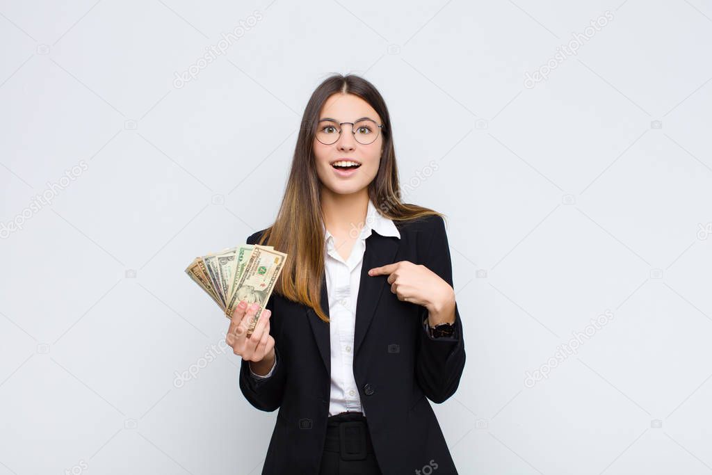 young pretty woman feeling happy, surprised and proud, pointing to self with an excited, amazed look with banknotes