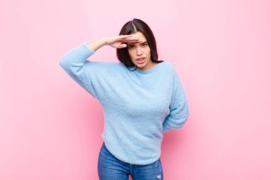 Genç, güzel bir kadın şaşkınlık ve şaşkınlık içinde bakıyor. Alnı açık, uzaklara bakıyor. Pembe duvara bakıyor ya da onu arıyor.