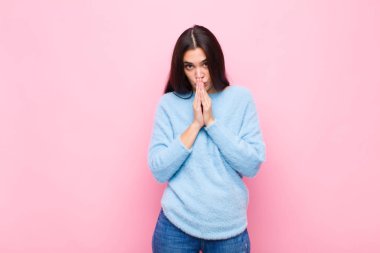 Genç, güzel bir kadın endişeli, umutlu ve dindar, avuçlarına bastırılmış bir şekilde dua ediyor, pembe duvara karşı af diliyor.