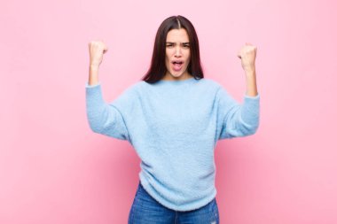 Genç ve güzel bir kadın inanılmaz bir başarıyı kutluyor. Kazanan gibi, heyecanlı ve mutlu görünüyor. Al bakalım! Pembe duvara yaslan