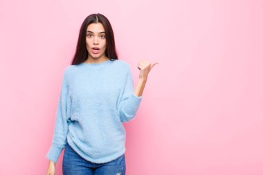 Genç ve güzel bir kadın inançsızlıktan şaşkın şaşkın bakıyor, yan taraftaki objeyi işaret ediyor ve diyor ki vay be, pembe duvara karşı inanılmaz.