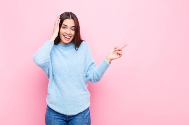 Genç, güzel bir kadın gülüyor, mutlu, pozitif ve şaşırmış görünüyor. Pembe duvara karşı yanal fotokopi alanını göstererek harika bir fikir olduğunu fark ediyor.