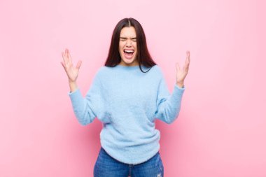 Genç ve güzel bir kadın öfkeyle bağırıyor, stresli hissediyor ve ellerini havaya kaldırıp neden pembe duvara yaslandığımı söylüyor.
