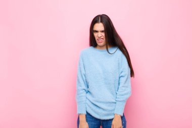 Genç ve güzel bir kadın şaşkın ve şaşkın hissediyor, aptal, şaşkın bir yüz ifadesiyle beklenmeyen bir şeye bakıyor pembe duvara karşı.