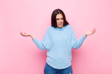 Genç, güzel bir kadın aptal, deli, kafası karışık, şaşkın bir ifadeyle omuz silkiyor. Pembe duvara karşı sinirli ve cahil hissediyor.