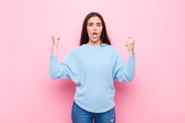 Genç ve güzel bir kadın sinirli bir ifadeyle ya da pembe duvara karşı başarıyı kutlayan yumruklarla agresif bir şekilde bağırıyor.