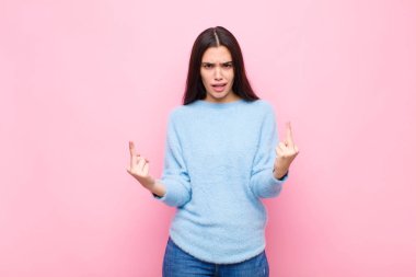 Genç ve güzel bir kadın kışkırtıcı, agresif ve müstehcen hissediyor, pembe duvara karşı isyankar bir tavırla orta parmağını hareket ettiriyor.