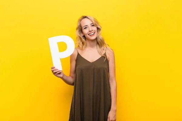 young blonde woman excited, happy, joyful, holding the letter Q of the alphabet to form a word or a sentence.
