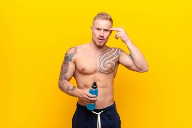 Genç sarışın güçlü bir adam kafası karışık ve şaşkın hissediyor, deli olduğunu ya da enerji içeceğiyle aklını kaçırdığını gösteriyor.