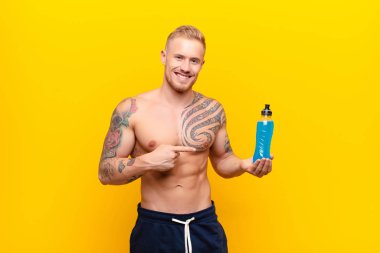 Genç, sarışın, güçlü, gülümseyen, mutlu, kaygısız ve tatmin olmuş bir adam, fotokopi alanındaki konsepte veya fikre bir yandan enerji içeceğiyle işaret ediyor.