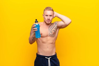 Genç sarışın güçlü bir adam stresli, endişeli, endişeli ya da korkmuş, elleri başının üstünde, bir enerji içeceğiyle yanlışlıkla panikliyor.