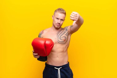 Genç sarışın, güçlü, sinirli, sinirli, hayal kırıklığına uğramış ya da hoşnutsuz bir genç. Boks eldivenleriyle ciddi bir bakış atıyor.