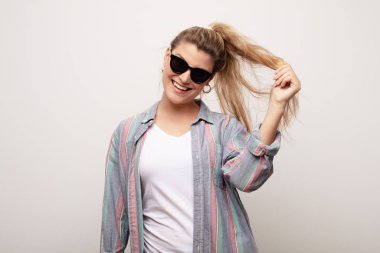 Düz duvara dayanmış, güneş gözlüğü takan genç Latin bir kadın.