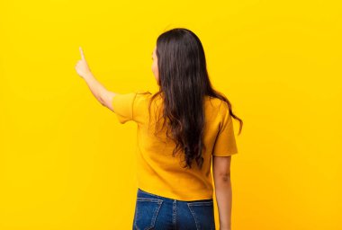 Fotokopi alanında duran ve objeye işaret eden genç Latin güzel kadın, düz duvara karşı dikiz penceresi