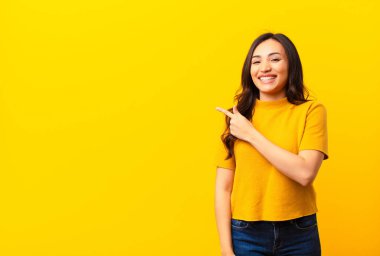 Genç Latin güzel kadın heyecanlı ve şaşırmış görünüyor. Yana ve yukarıya doğru düz duvara uzayı gösteriyor.