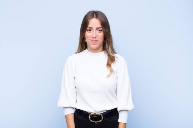 Genç ve güzel İspanyol kadın pozitif ve kendinden emin gülümsüyor, memnun görünüyor, arkadaş canlısı ve mavi duvara karşı mutlu.