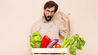 Yeşil market sahibi mutsuz ve stresli görünüyor, intihar jesti elle silah işareti yapıyor, kafasını işaret ediyor.