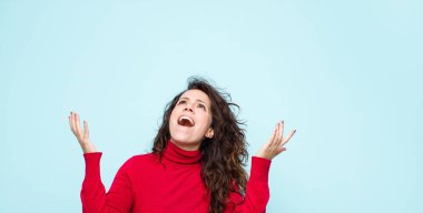 Genç, güzel bir kadın kendini mutlu, şaşkın, şanslı ve şaşırmış hissediyor. Zaferi kutlarken iki elini de havaya kaldırıp mavi duvara yaslanıyor.