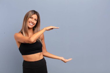 Genç, güzel bir kadın gülümsüyor, mutlu, pozitif ve tatmin olmuş hissediyor, fotokopi alanında nesne veya konsept tutuyor veya gösteriyor