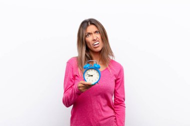 Genç güzel kadın şaşkın ve şaşkın hissediyor, aptal, afallamış bir ifadeyle beklenmeyen bir şeye bakıyor çalar saat tutuyor..