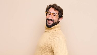 Genç havalı adam mutlu, neşeli ve kendinden emin görünüyor, gururla gülümsüyor ve kalçalarını yassı duvara dayayıp iki elini de kaldırmayı bekliyor.