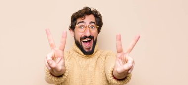 Genç, havalı bir adam gülümsüyor ve mutlu görünüyor, arkadaş canlısı ve memnun, iki elini de duvara dayayıp zafer ya da barış işareti yapıyor.