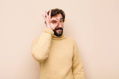 Genç havalı adam mutlu bir şekilde gülümsüyor, şaka yapıyor ve gözetleme deliğinden bakıyor, düz duvara karşı sırları gözetliyor.