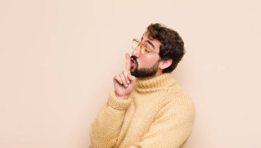 Havalı genç adam ciddi görünüyor ve parmaklarını dudaklarına bastırıp sessizlik ya da sessizlik talep ediyor, düz duvara karşı bir sır saklıyor.