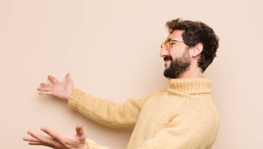 Genç, havalı bir adam neşeyle gülümsüyor sıcak, dostça, sevgi dolu bir kucaklama yapıyor, mutlu ve sevimli hissediyor düz duvara karşı.