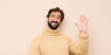 Genç havalı adam mutlu ve neşeyle gülümsüyor, el sallıyor, seni selamlıyor, ya da düz duvara karşı veda ediyor.