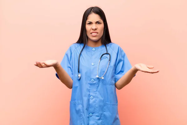 young latin nurse feeling clueless and confused, not sure which choice or option to pick, wondering against pink wall