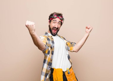 young housekeeper man shouting triumphantly, looking like excited, happy and surprised winner, celebrating against flat wall