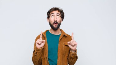 Genç ve yakışıklı bir adam şaşkınlık içinde ve ağzı açık bir şekilde yukarı bakıyor ve şaşırmış bir şekilde düz duvara bakıyor.