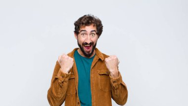 Genç yakışıklı adam muzaffer bir şekilde bağırıyor, gülüyor, mutlu ve heyecanlı hissederken düz duvara karşı başarıyı kutluyor.