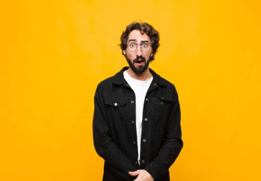 Genç çılgın yakışıklı adam korkmuş ve şok olmuş hissediyor, ağzı açık turuncu duvara karşı şaşkınlık içinde.