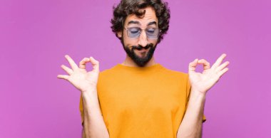 Genç çılgın adam konsantre ve meditasyon yapıyor, tatmin olmuş ve rahatlamış, düşünüyor ya da düz duvara karşı bir seçim yapıyor.