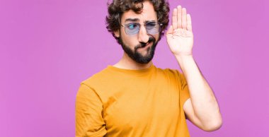 Genç çılgın adam ciddi ve meraklı görünüyor, dinliyor, gizli bir konuşma ya da dedikodu duymaya çalışıyor, düz duvara kulak misafiri oluyor.