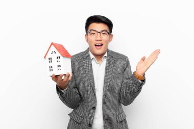 Genç Japon adam mutlu, heyecanlı, şaşırmış ya da şok olmuş hissediyor. Bir ev modeliyle inanılmaz bir şeye gülümsüyor ve hayrete düşüyor.