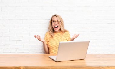 Genç sarışın kadın mutlu, heyecanlı, şaşırmış ya da şaşırmış hissediyor, gülümsüyor ve hayrete düşüyor.