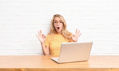 Genç sarışın kadın şok olmuş, şaşırmış ve şaşırmış hissediyor. Onaylıyor. İki eliyle de dizüstü bilgisayar kullanarak imza atıyor.