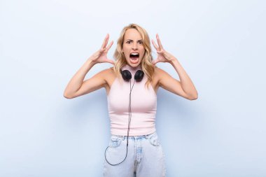 Genç sarışın kadın elleri havada bağırıyor, öfkeli, sinirli, stresli ve üzgün hissediyor müzik dinliyor.